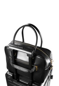 Schwarze Reisetasche aus Leder mit zwei oberen Griffen, goldenen Reißverschlüssen und Logo-Riemen. Verfügt über einen Teleskopgriff und eine strukturierte Außenseite.