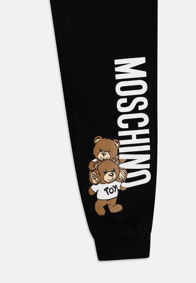 Μαύρο φόρεμα με σχέδιο αρκούδας που απεικονίζει δύο στοιβαγμένες αρκούδες, η μία φοράει ένα λευκό μπλουζάκι με την ένδειξη "TOY" και το λογότυπο "MOSCHINO" σε έντονο λευκό κείμενο.