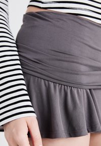 Šedá zavinovací sukně s rozšířeným lemem, vyrobená z měkké tkaniny, spojená s černobílým pruhovaným topem s dlouhým rukávem a přiléhavými manžetami.