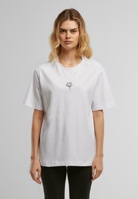 Tricou alb din bumbac cu un design al unei flori de lotus desenate cu linii negre pe piept, cu mâneci scurte și un croi lejer.