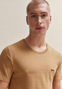 T-shirt en coton marron avec un col rond et des manches courtes. Présente un logo "BOSS" brodé sur le côté gauche de la poitrine.