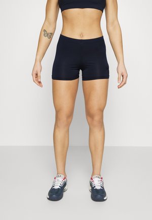Shorts de sport bleu marine et un crop top, tous deux en tissu lisse. Portant des baskets bleu marine avec des lacets blancs et des accents rouges.