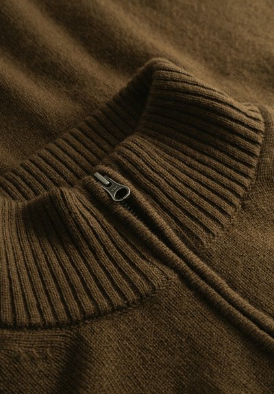Pull en tricot marron avec un col haut côtelé et une fermeture éclair métallique partiellement fermée avec la marque YKK.