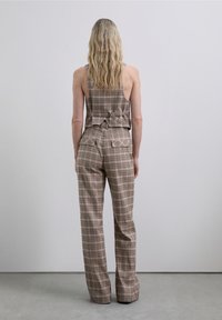 Brunternetternettet ærmeløs top med en sløjfe detalje på ryggen, parret med matchende højtaljede bukser med laplommer.