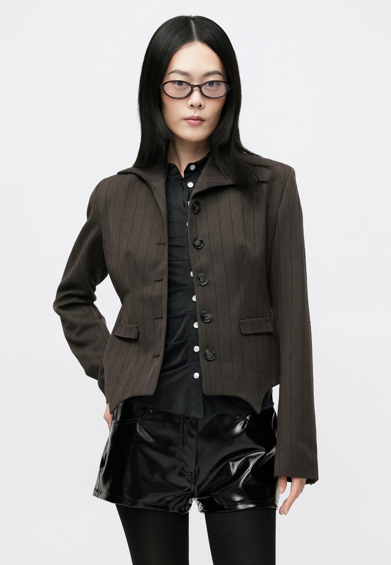 Brun rillede skræddersyet jakke med struktureret krave, frontknapper og to klaplommer, parret med skinnende sorte shorts.