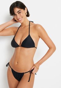 Juodas bikini komplektas su trikampio formos viršumi ir reguliuojamais šonais. Piduri švelni medžiaga, minimalistiškas dizainas ir lengvas konstrukcija.