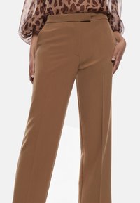 Pantaloni marroni su misura con una texture liscia, design a gamba dritta, tasche laterali e vita cinte per una vestibilità strutturata.