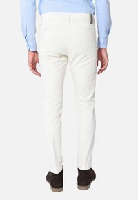 Pantaloni bianchi su misura in cotone, con vestibilità slim, tasche laterali e un design pulito sul retro, abbinati a scarpe in suede marroni.