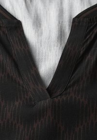 Tissu noir avec un motif brun foncé subtil, présentant un design en V et des détails de bande contrastants au niveau de l'encolure.