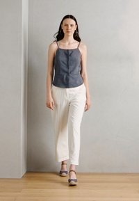 Top de denim sin mangas con un diseño ajustado, combinado con pantalones de pierna ancha a rayas claras y sandalias grises. Fondo neutro y suelo de madera.