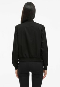 Zwarte bomberjack met een cropped ontwerp, ribgebreide tailleband en lange mouwen. Glad materiaal zonder zichtbare patronen of hardware.