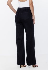 Czarne dżinsy o luźnym kroju, z elastycznym pasem i dwiema tylnymi kieszeniami, charakteryzujące się gładką strukturą i prostym krojem nogawek.