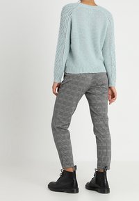 Jasnoniebieski dziergany sweter z teksturowanymi rękawami, zestawiony z szarymi spodniami do kostek w kratę i czarnymi sznurowanymi botkami.