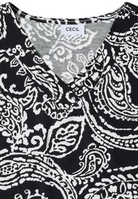 Tissu à motif cachemire noir et blanc avec un col en V et une étiquette de marque "CECIL" cousue à l'intérieur de l'encolure.