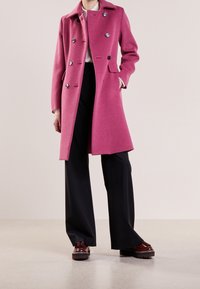 Roze wollen jas met een dubbelzijdig ontwerp, zilveren knopen, notch kraag, zijzakken, gecombineerd met zwarte wijde broek en platform schoenen.