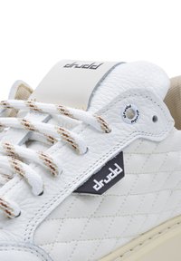 Biały skórzany sneaker z pikowaną teksturą, brązowymi i beżowymi akcentami, naszywką z logo na języku oraz wielokolorowymi plecionymi sznurówkami. Gumowa podeszwa.