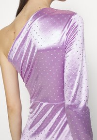 Femme portant une robe en velours lavande à une épaule avec des ornements en strass sur la manche et le corsage, montrant le dos et l'épaule.