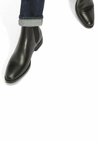 Botas Chelsea de cuero negro con un upper liso, punta afilada, paneles laterales elásticos y un tacón bajo apilado, combinadas con denim enrollado.