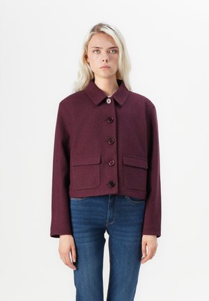 Burgundy cropped jacket made of textured fabric, featuring a collar, button closure, and two front pockets. Worn over blue jeans.