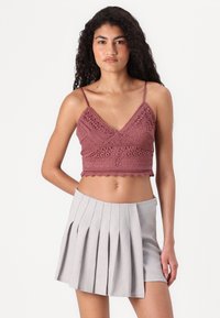 Heklet bralette i mauve med V-hals og delikate blonderdetaljer, sammen med en hellang lys grå nederdel med plisseringer og glidelås på siden.