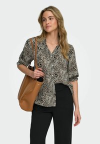 Blusa de estampado de leopardo con mangas cortas, frente abotonado, cuello estructurado; combinada con pantalones negros y un bolso de tote de cuero marrón.