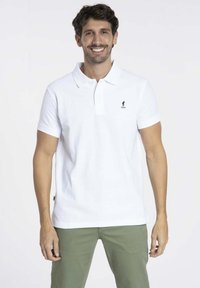 Polo shirt blanc  à manches courtes avec un col classique et un petit logo brodé sur la poitrine. Associé à un pantalon vert olive.