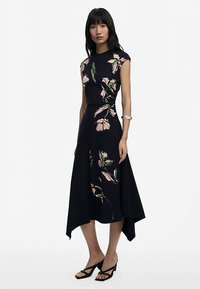 Mėlynos spalvos su gėlių raštais suknelė be rankovių, asimetriško kirpimo apdaila. Pasižymi rožiniais ir žaliais akcentais ant lygaus audinio. Paprastos stiliaus dirželinės basutės.