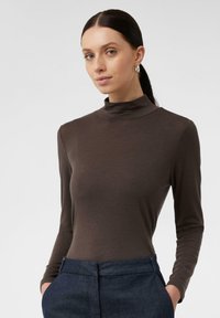 Brauner langärmliger Rollkragenpullover aus weich anliegendem Material. Minimalistisches Design mit glatter Textur, kombiniert mit dunklen, taillierten Hosen.