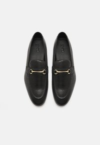 Black loafers made of textured leather, featuring a gold-tone chain accent and a smooth toe box. Simple and classic design.