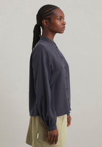 Blusa a maniche lunghe blu navy con colletto alto, chiusura anteriore con bottoni e maniche arricciate. Tessuto morbido con vestibilità rilassata.