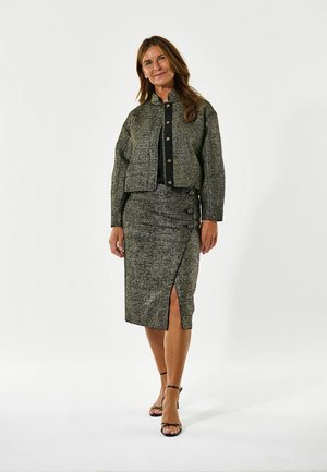 Musta ja kultainen teksturoitu lyhyt takki nappikiinnityksellä yhdistetty midi-hameeseen, jossa on sivuhalkio ja nappikoristukset. Mustat korkokengät.