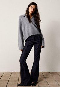 Grå stickad tröja med krage, kombinerad med mörka randiga utsvängda byxor. Svarta ballerina skor fulländar outfiten.