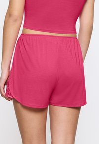 Fuksjowe spodenki sportowe z elastycznym pasem, miękkim materiałem, bocznymi rozcięciami i zdobieniem koronkowym na krawędzi dla dodatkowej tekstury.