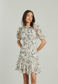 Blumenkleid mit kurzen Puffärmeln, elastischem Bund und gerüschtem Saum. Leichter Stoff mit grünen Blättern und rosa Blumen auf einem cremefarbenen Hintergrund.