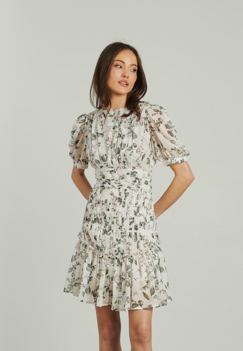 Blumenkleid mit kurzen Puffärmeln, elastischem Bund und gerüschtem Saum. Leichter Stoff mit grünen Blättern und rosa Blumen auf einem cremefarbenen Hintergrund.