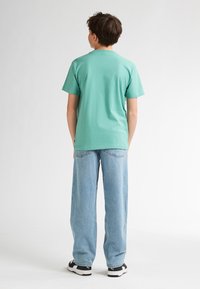 Muntgroen katoenen T-shirt, korte mouwen, losse pasvorm, gecombineerd met lichtblauwe jeans met wijde pijpen en zwarte sportschoenen. Eenvoudig ontwerp.