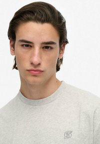 Graues Baumwoll-T-Shirt mit Rundhalsausschnitt, einem kleinen, bestickten Logo auf der linken Brust, glatter Textur und entspannter Passform.