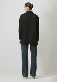 Zwarte shirt met kraag, lange mouwen, relaxte pasvorm, gebogen zoom, gecombineerd met blauwe denim jeans en witte sneakers.