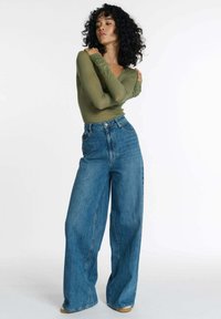 Groene lange mouwen top gecombineerd met hoge taille, wijde blauwe jeans. De denim heeft een licht gewassen look, met een gladde textuur en minimale details.