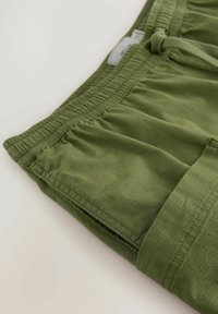 Pantalon en tissu léger vert olive avec ceinture élastique et cordon de serrage, montrant un gros plan des détails de la poche cousue et de la ceinture.