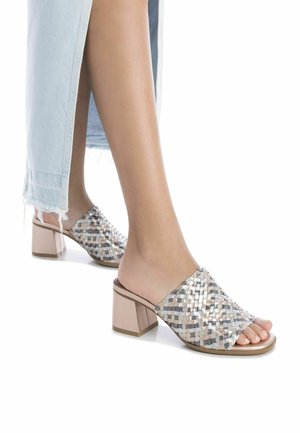 Sandalias deslizantes tejidas que presentan una mezcla de tonos metálicos plateados y beige, con un tacón cuadrado y diseño de punta abierta.