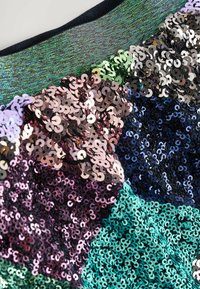 Primo piano di un tessuto con paillettes iridescenti cucite densamente nei colori pastello rosa, verde, blu, argento e viola, creando un effetto patchwork scintillante.