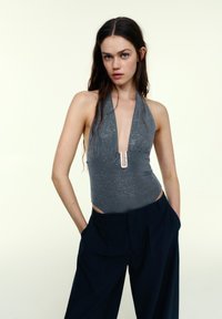 Szary kostium kąpielowy na szyję z błyszczącymi detalami i głębokim dekoltem w kształcie litery V. Dobry do wysokich, ciemnogranatowych spodni z wysokim stanem. Bez widocznych wzorów.