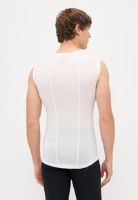 Hvid ærmeløs skjorte med et tekstureret netstof, der har en tætsiddende design og kontrasterende syninger, båret af en model set fra ryggen.