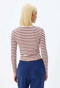 Langarmtop met bordeauxrode en crèmekleurige strepen, aansluitend ontwerp, zachte katoenstof. Gecombineerd met blauwe zweetbroeken met elastische taille.