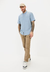 Lichtblauwe korte mouw overhemd met knoopsluiting en een borstzak, gecombineerd met kaki broeken en witte sneakers met donkere accenten.