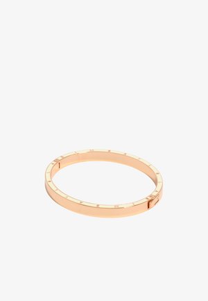 Náramok v tvare kruhu z ružového zlata s vyrytým názvom značky okolo vonkajšieho okraja a malou obdĺžnikovou sponou.