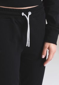 Czarne dresy z elastycznym pasem i sznurkiem, z białymi akcentami. Tkanina wydaje się miękka i gładka w dotyku.