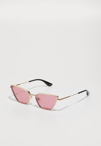 Triangular sunglasses with pink lenses, gold metal frame, and black plastic temples. Features a minimalist design and sleek lines.