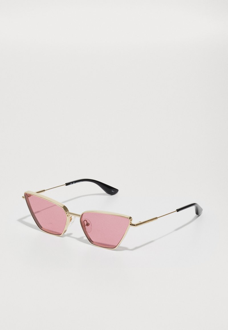 Kolmnurksed prillid roosa läätses, kuldmetallist raam ja mustast plastist rööpad. Omab minimalistlikku disaini ja voolujooni.